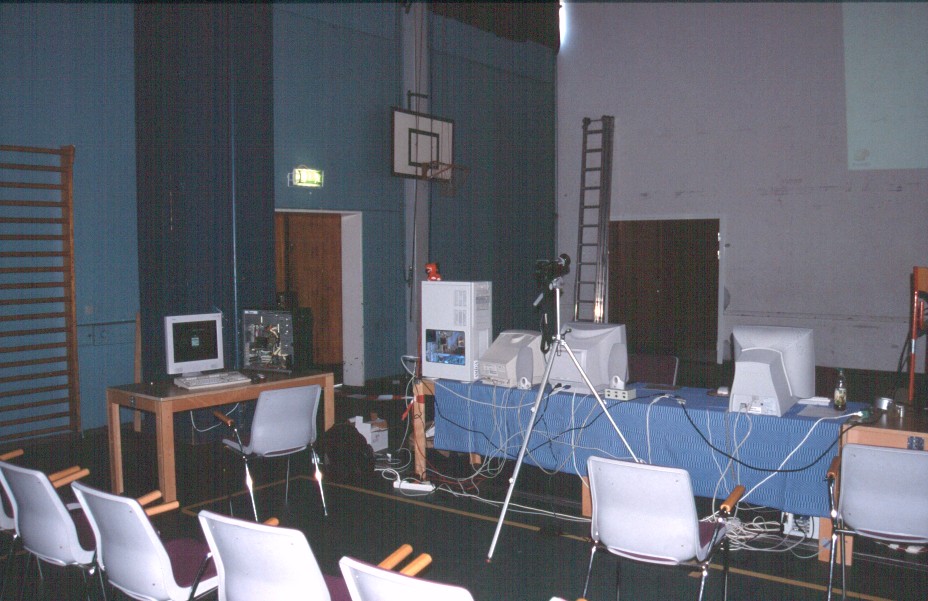 2: The plain and simple setup for the event: Justin's AmigaOne table at the left, and Peter's and my own A4ks on the long table, taking turns on the data projector (on the chair to the far right). Jens' DV camera in the foreground.